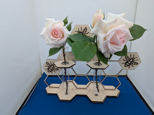 Double bud vase with laser-cut honeycomb and bee design holding pale pink roses in glass test tubes.